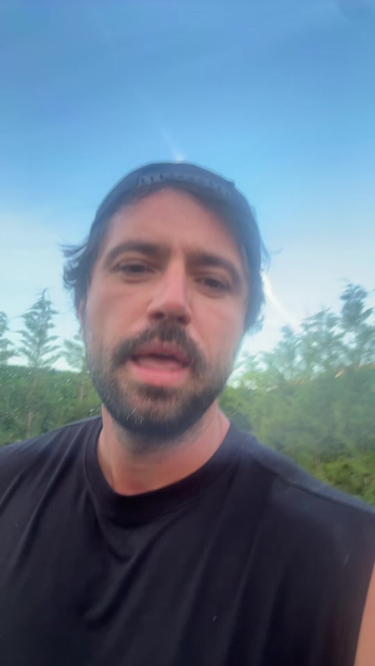 Eduard in a black T-shirt speaking outdoors under a blue sky, with trees behind him.