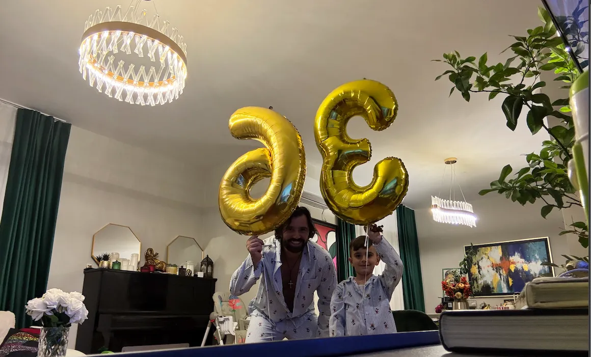 Man and young boy in pajamas holding gold number 36 balloons at home
