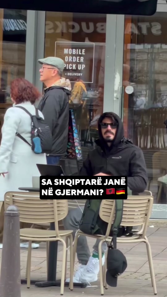 Eduard outside a café in the original video, with Albanian text asking how many Albanians live in Germany.