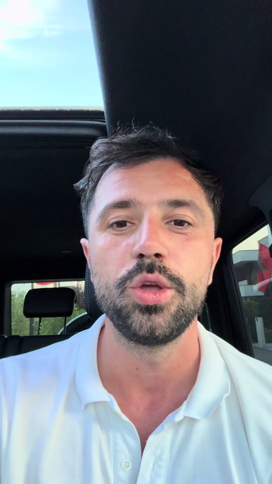 Eduard wearing a white polo shirt, speaking to the camera inside a car.