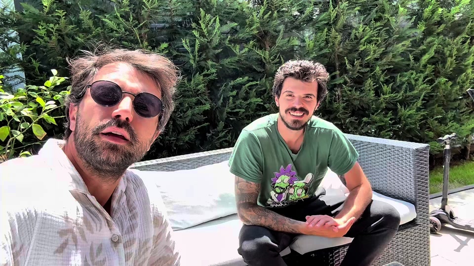 Eduard in sunglasses sitting outdoors beside his brother in a green T-shirt.