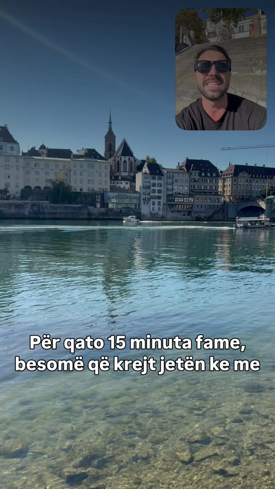 The river and waterfront buildings in Basel, with Eduard wearing sunglasses in an inset and Albanian subtitles across the lower image.