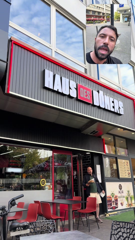 A Haus des Döners storefront with red chairs and a large white-and-red sign, with Eduard speaking in the original video inset.