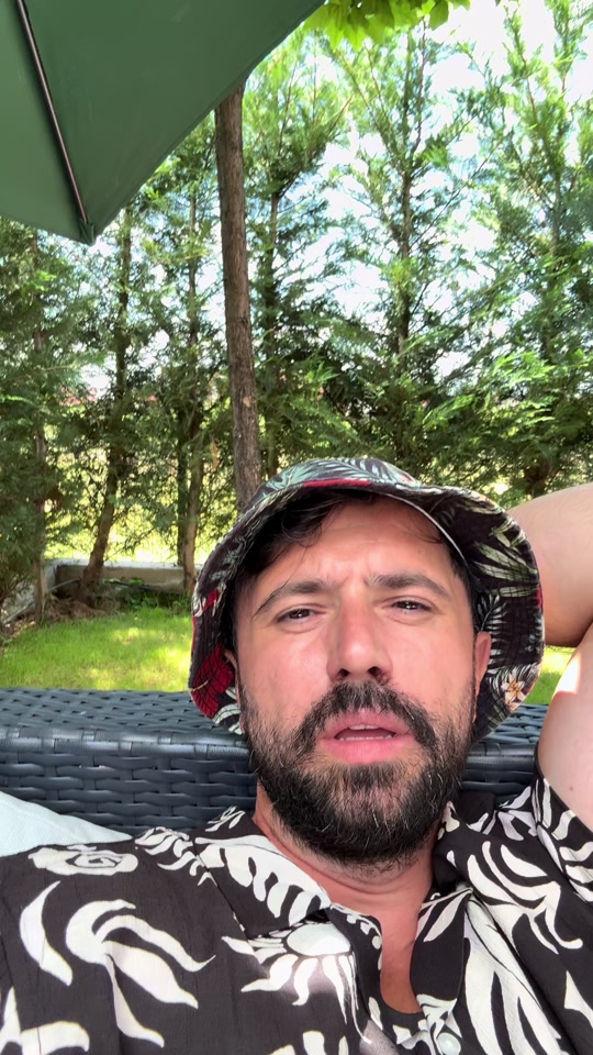 Eduard reclining outdoors in a garden chair, wearing a bucket hat, in the original video about healing and avoidance.