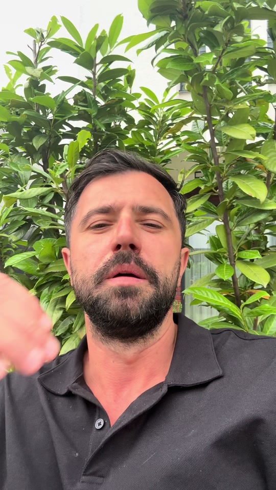 Eduard outdoors in a black polo shirt with green leaves behind him, in the original video about honesty.