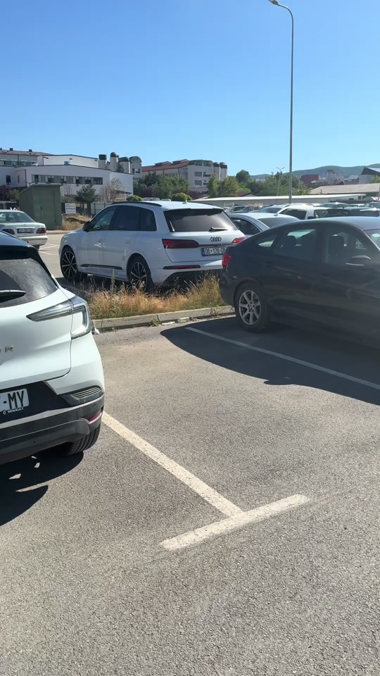 An empty marked parking bay among parked cars on hospital grounds, seen in the original video.