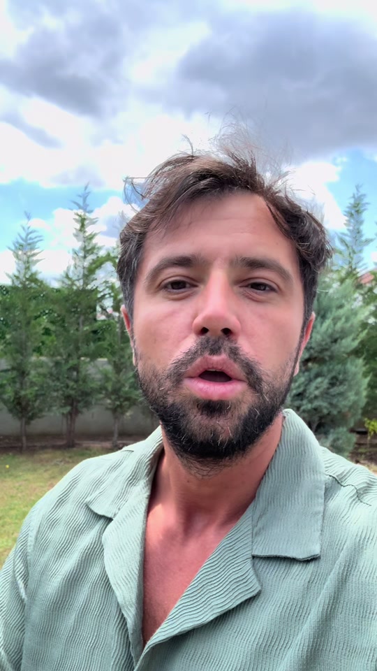 Eduard in a pale green shirt speaking outdoors, with trees and a cloudy sky behind him.