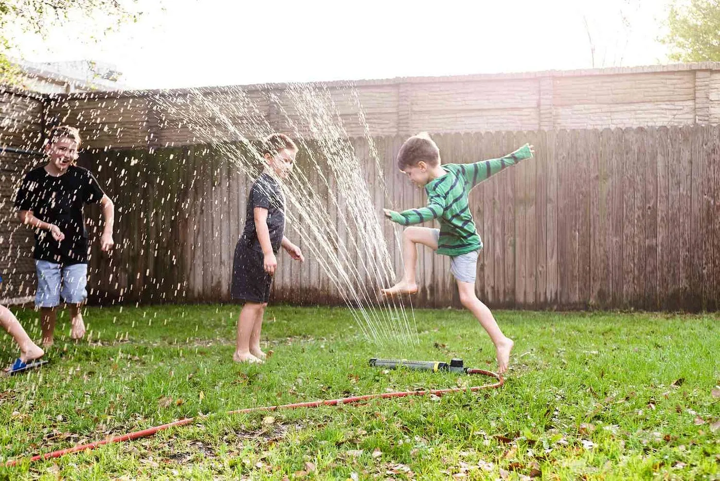 Children joyfully leaping through a garden sprinkler on a sunny backyard lawn