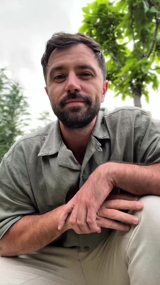 Eduard sitting outdoors in a green shirt, with trees behind him