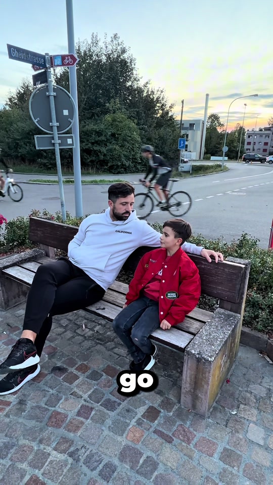 Original video thumbnail of an adult and a child in a red jacket sitting together on a wooden bench outdoors.