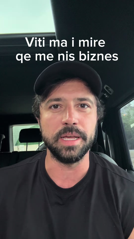 Eduard in a black shirt and cap inside a car, under the original Albanian caption about starting a business.
