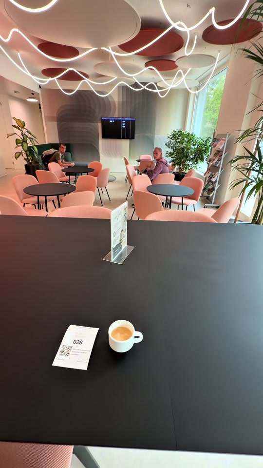 Original video cover showing a Swiss café with curved ceiling lights, pink chairs and a cup on a table.