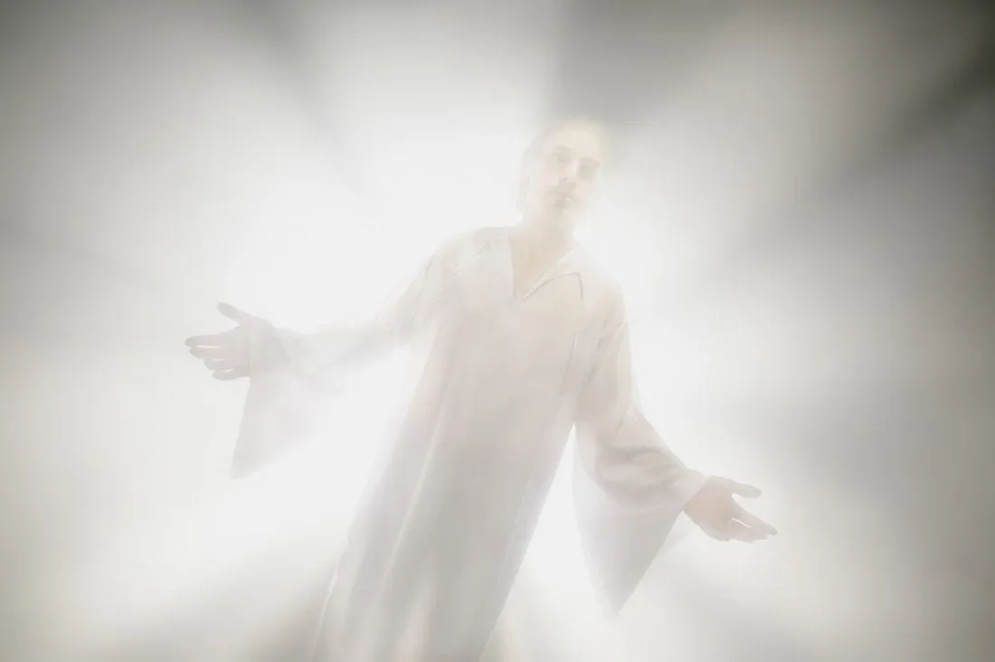Ethereal figure in a white robe, arms outstretched, dissolving into blinding light