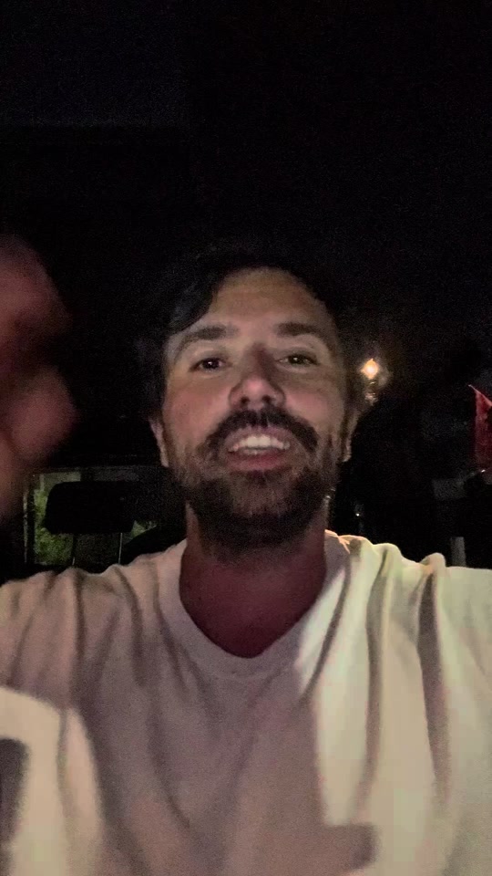 Eduard gesturing while speaking at night in a white T-shirt.