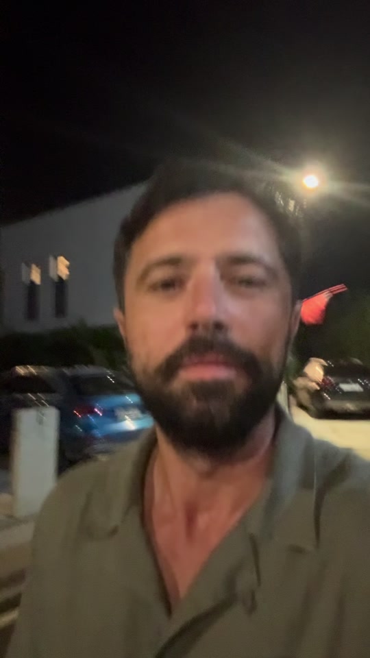 Eduard speaking outdoors at night in an olive shirt, with parked cars and a streetlight behind him.